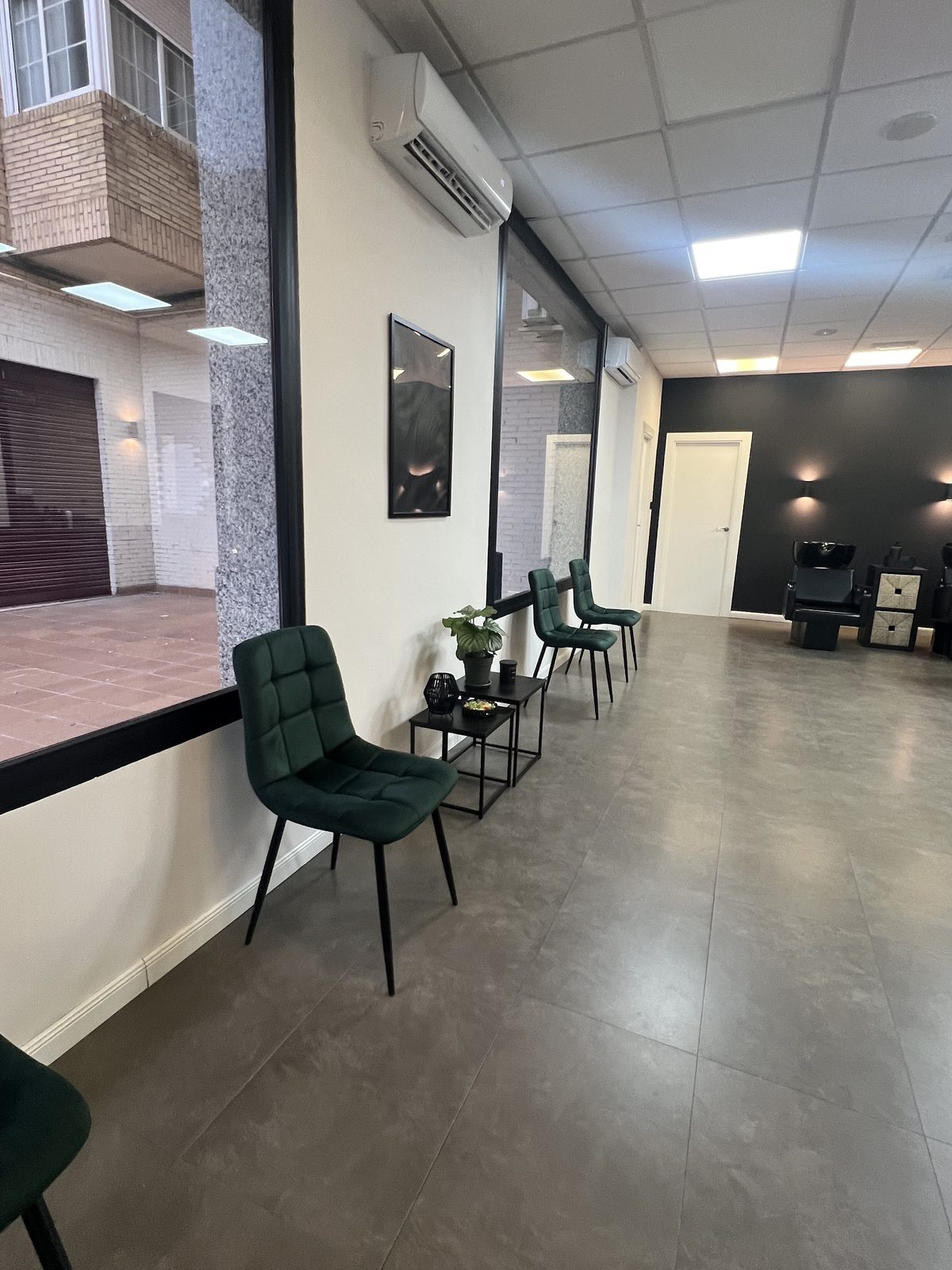 Zona de espera con sillas verdes junto a la ventana de la barbería